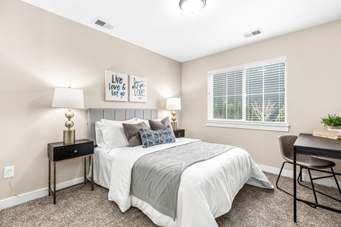 A bedroom with a bed, a chair, and a table with a lamp on it.