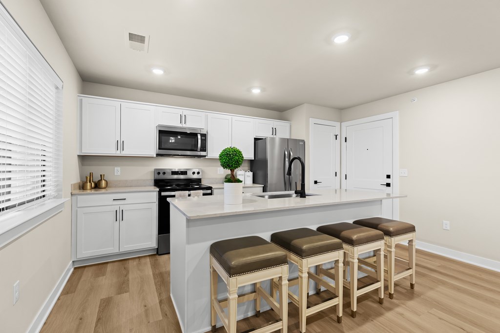 A kitchen with white cabinets and a white island with three stools.