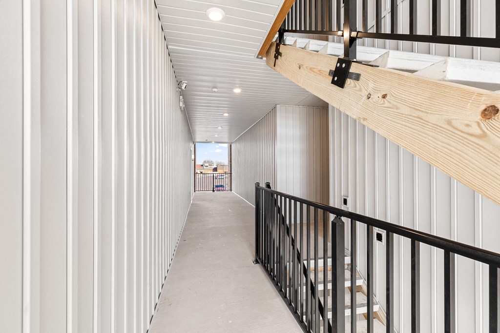 a long hallway with white walls and a staircase with wood and metal railing
