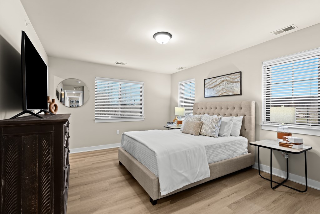 A bedroom with a large bed, a TV on a wooden stand, and a small table with books.