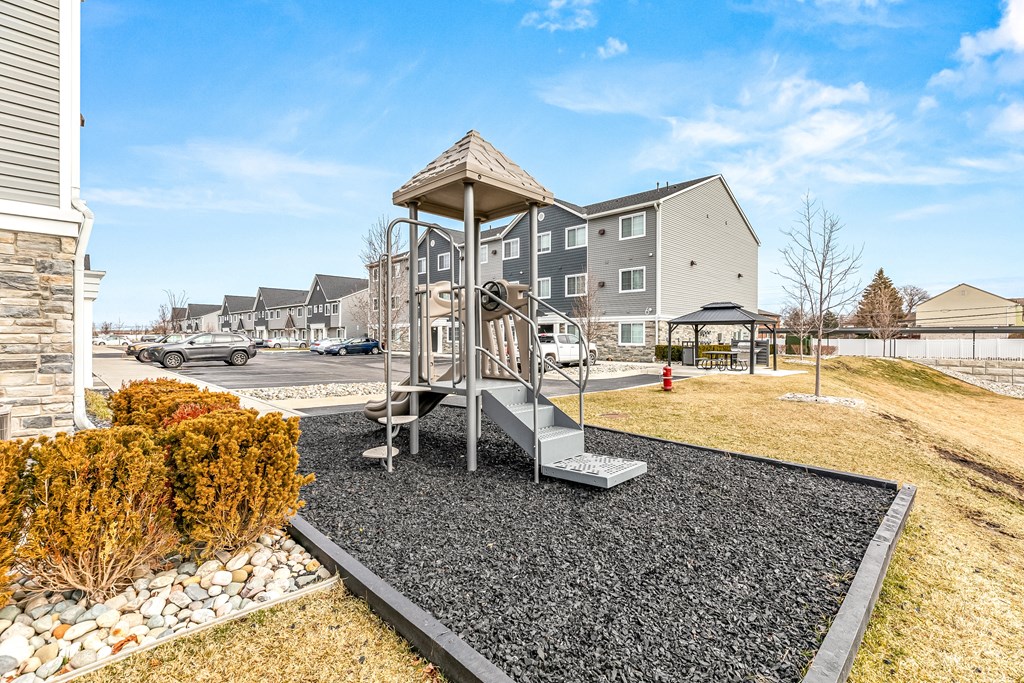 A playground with a slide and a swing set in the foreground and apartment buildings in the background.