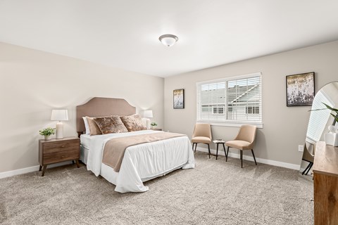 A bedroom with a large bed, two chairs, and a nightstand.