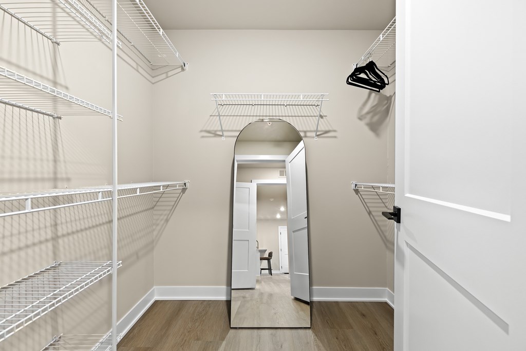 A walk-in closet with white shelving and a mirror.