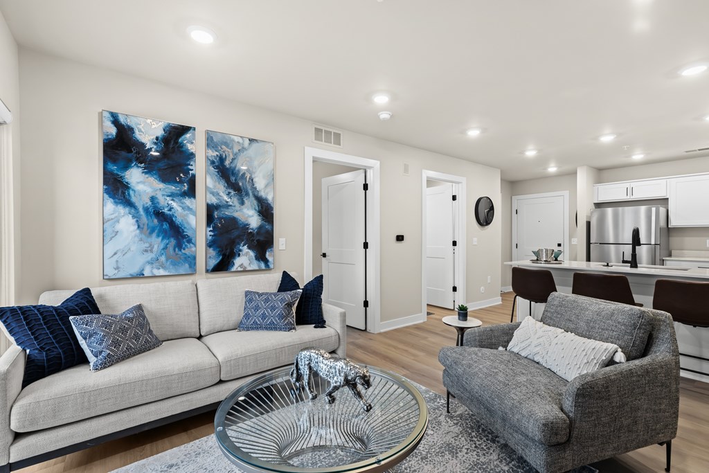 A modern living room with a grey couch, a glass coffee table, and a large abstract painting on the wall.