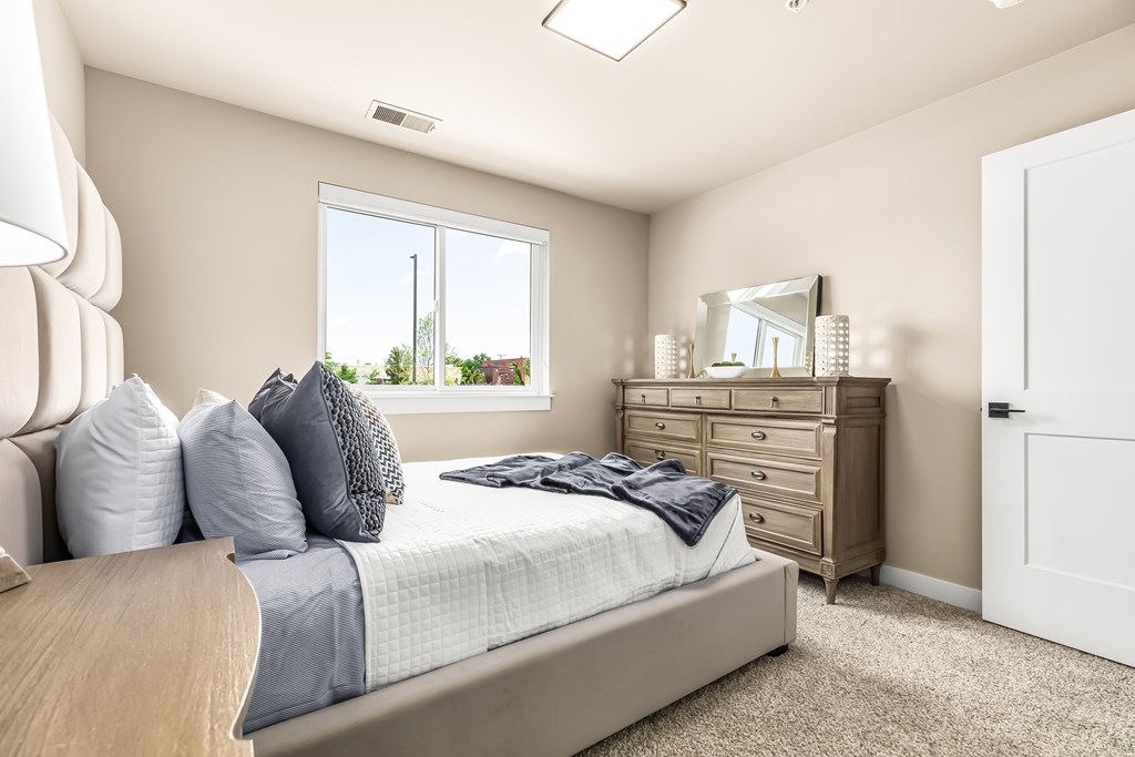 A bedroom with a bed, dresser, mirror, and window.