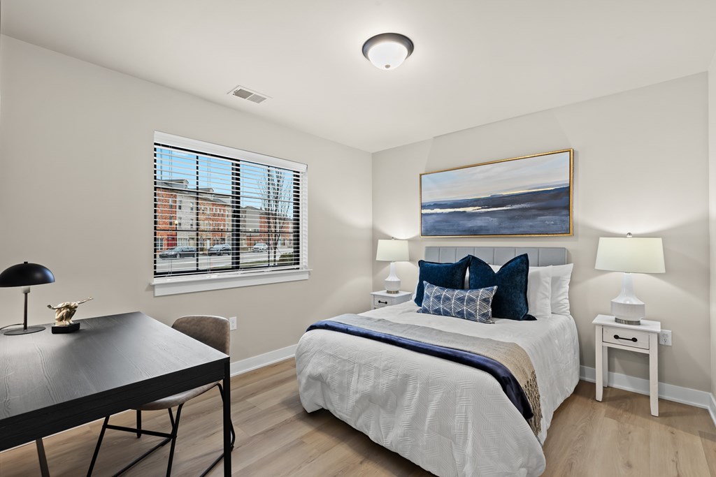 A bedroom with a bed, nightstand, and a painting on the wall.