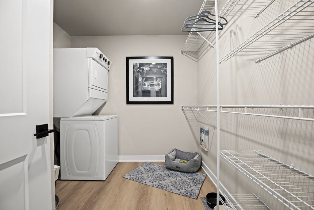 A white kitchen with a fridge, a trash can, a rug and a picture on the wall.