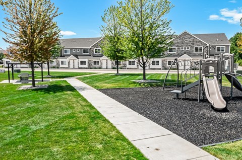 A playground with a slide and a walking path in front of a building.