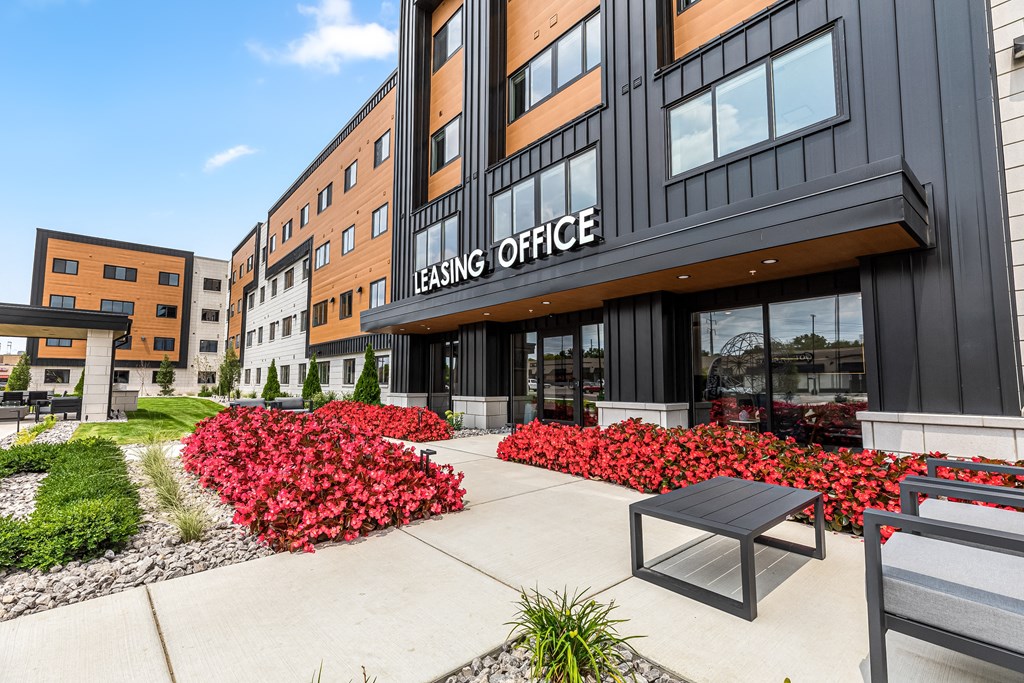 a walkway with benches and red flowers in front of a building