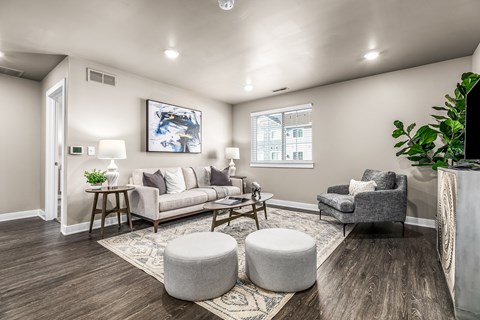A living room with a grey couch, a grey armchair, a grey ottoman, a wooden coffee table, and a painting on the wall.