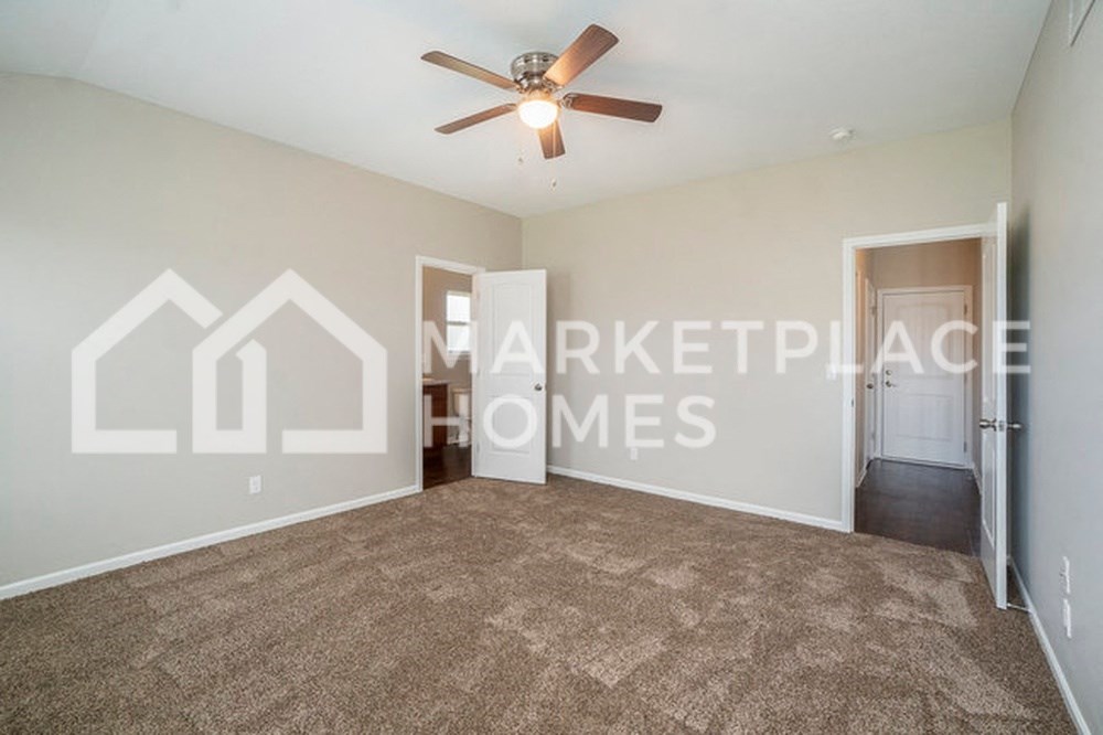 an empty living room with a ceiling fan and a door to a hallway