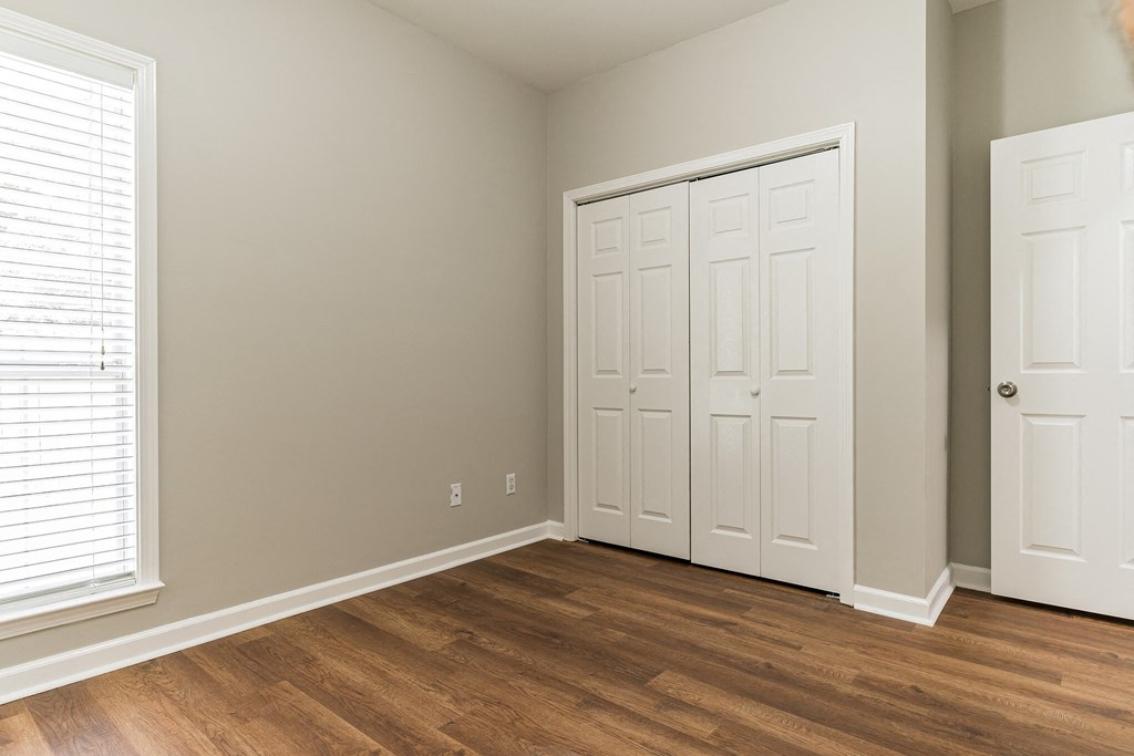 a bedroom with two closets and a window and wood floors
