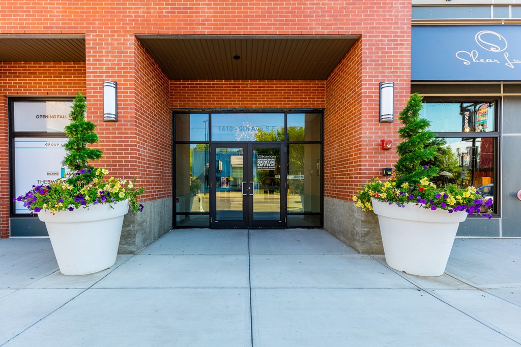 The front of a building with a glass door and two large planters with flowers.