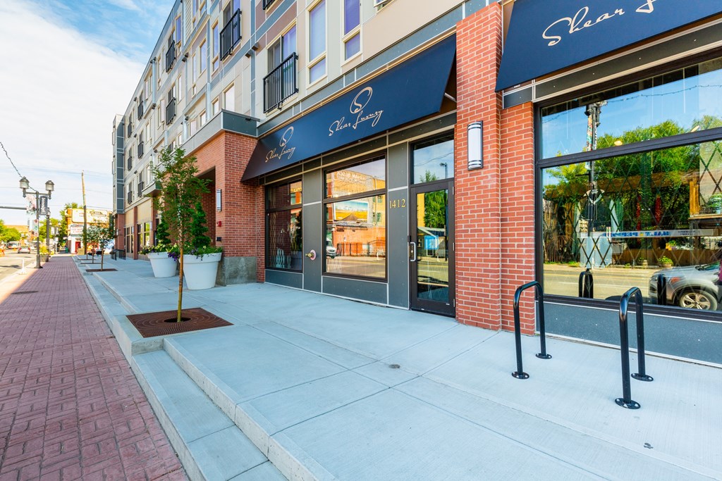 A brick sidewalk leads to a storefront with a blue awning.