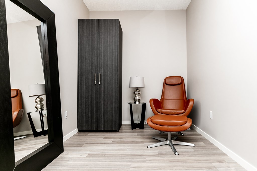 A brown leather chair sits in front of a tall cabinet in a room with a wooden floor.