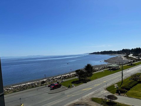 A red car is driving on a road near the ocean.