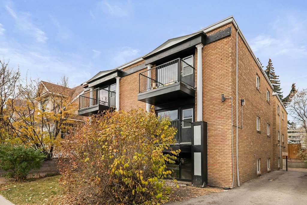 A red brick building with a balcony and a tree in front.