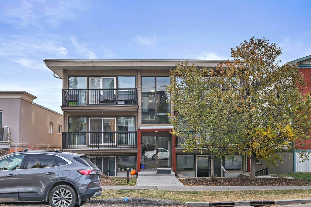 A modern two-story house with a balcony and a tree in front.
