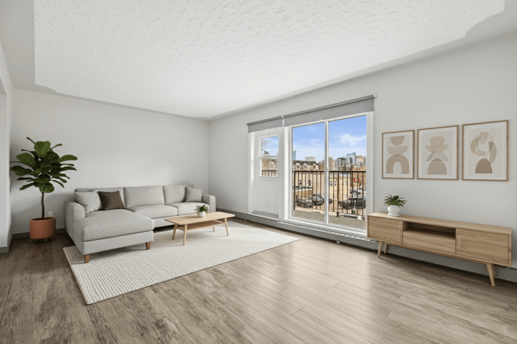 A living room with a grey sofa, a wooden coffee table, a potted plant, and a window with a view of the city.