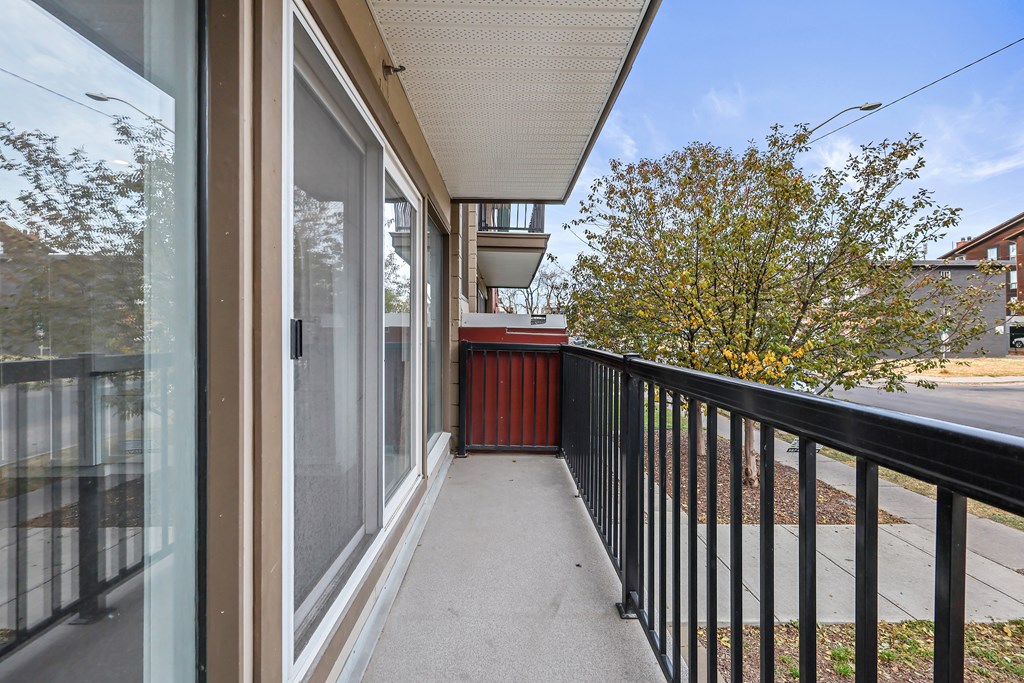 A balcony with a black railing and a view of a tree and a building.