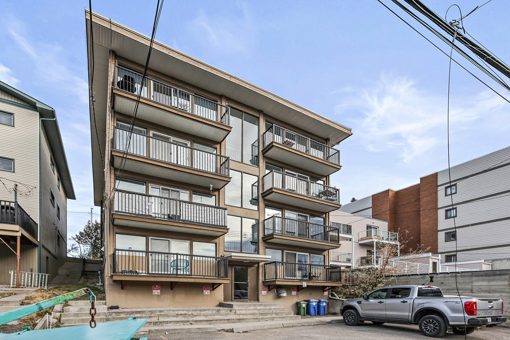 A silver truck is parked in front of a multi-story building.