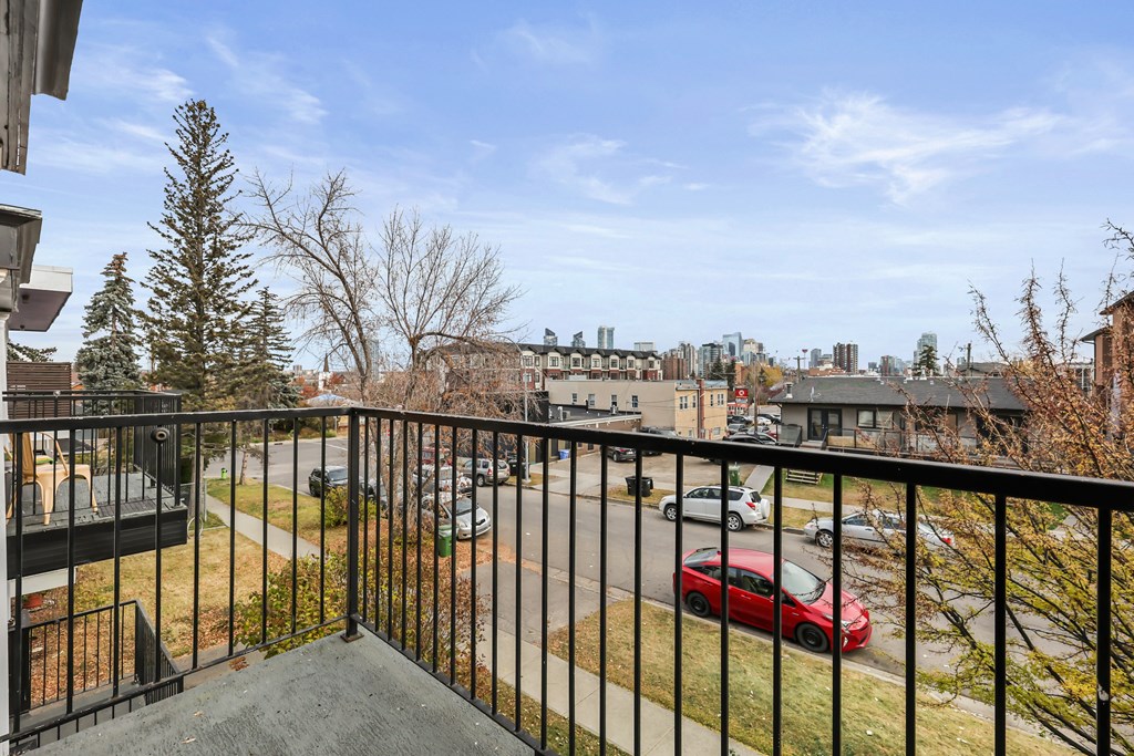 A red car is parked on the street below a balcony.