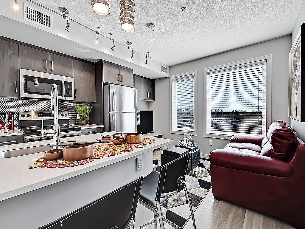 A modern kitchen with a red couch and black chairs.