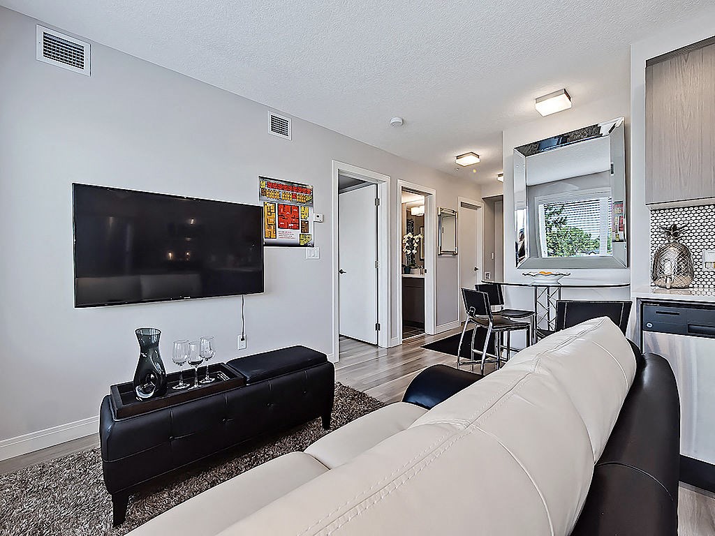 A black sofa with a white cushion is in the foreground of a well-lit living room.