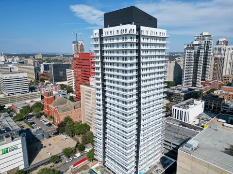 A tall building with a black top stands in the middle of a cityscape.