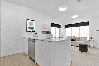 A modern kitchen with white cabinets and appliances, a framed picture on the wall, and a large window with blinds.