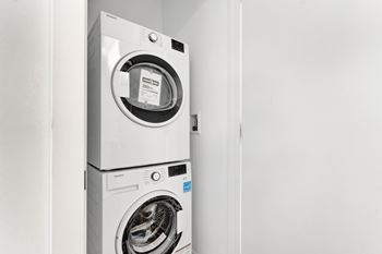 A white front loading washing machine with a black door is in a white room.