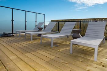 Two white chairs on a wooden deck with a glass railing.