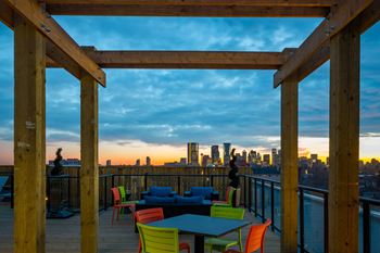 A wooden structure with a table and chairs in front of a city skyline at sunset.