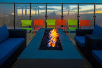 A fire pit sits in the middle of a blue table surrounded by colorful chairs.