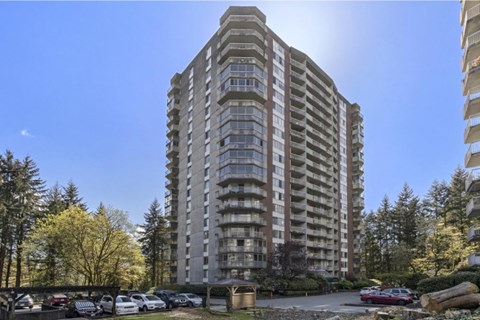 A tall residential building with a parking lot in front.