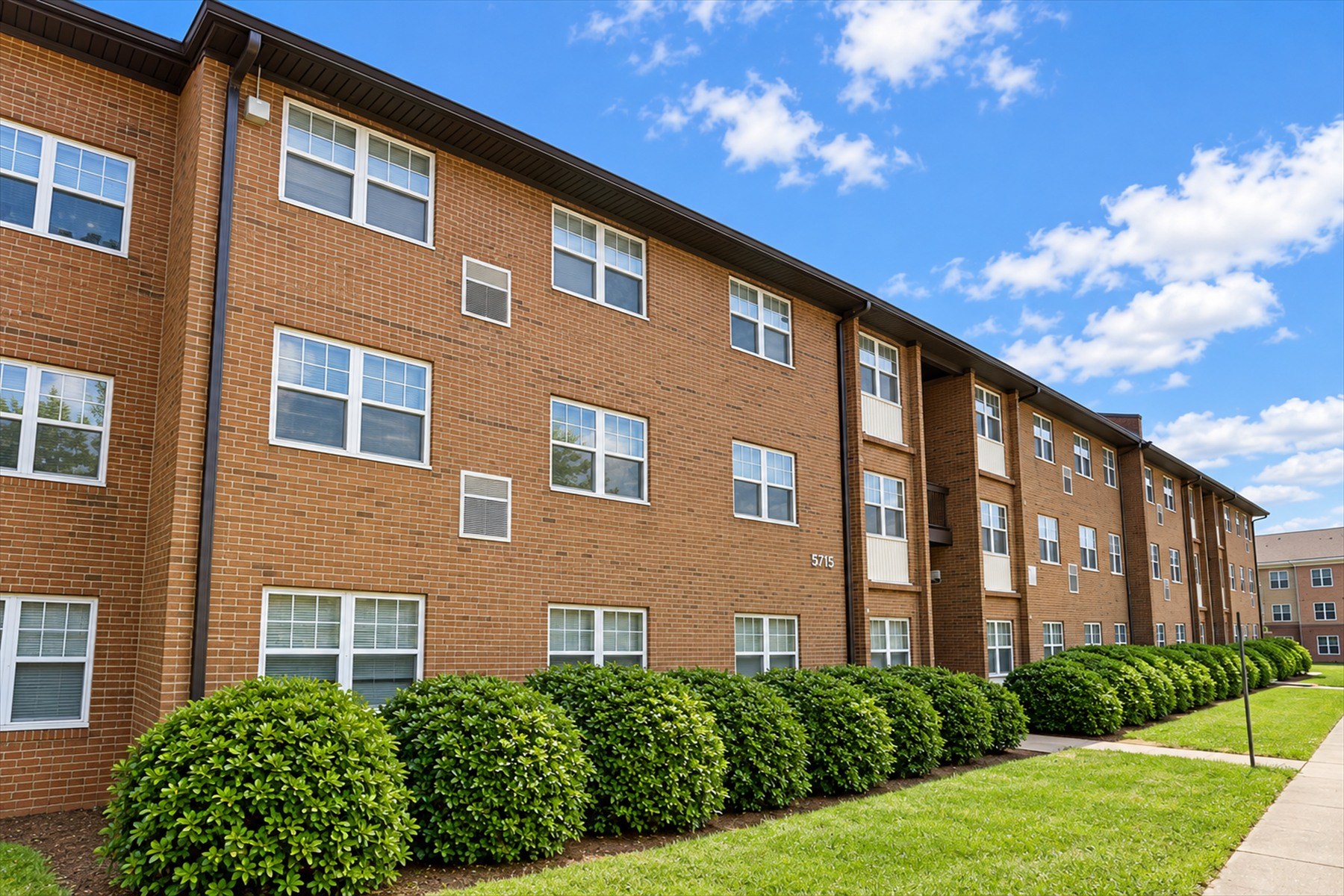 A row of red brick apartment buildings with green bushes in front.
