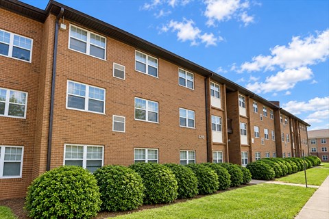 A row of red brick apartment buildings with green bushes in front.