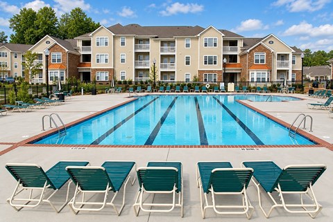 A swimming pool surrounded by lawn chairs in front of apartment buildings.