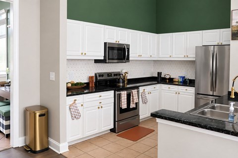 A kitchen with white cabinets and black countertops.