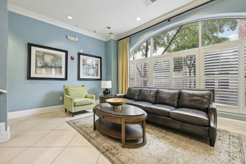 A living room with a black leather couch, a green chair, and two framed pictures on the wall.