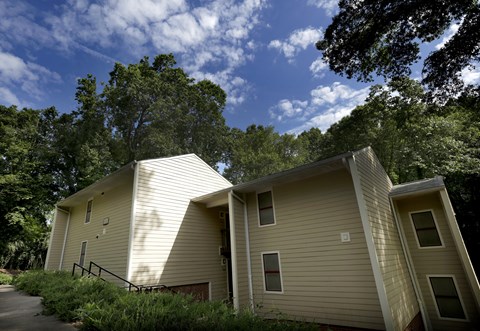 A beige house with a sloped roof is surrounded by trees.