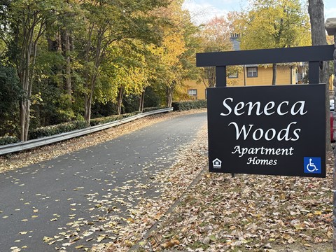 A sign for Seneca Woods Apartment Homes is shown in front of a tree-lined street.