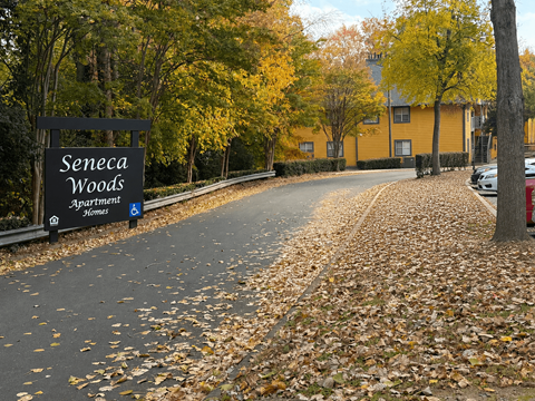 A black sign with white lettering that says Seneca Woods Apartment Homes.