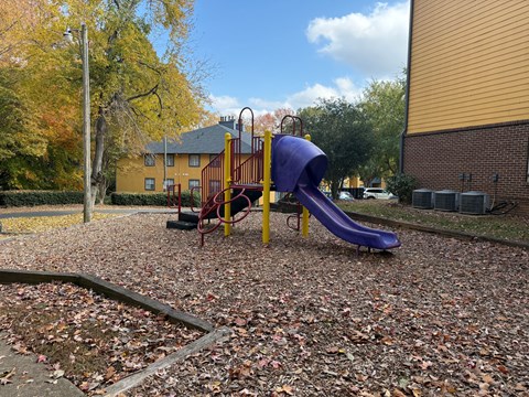 A playground with a purple slide and a yellow and red swing set.