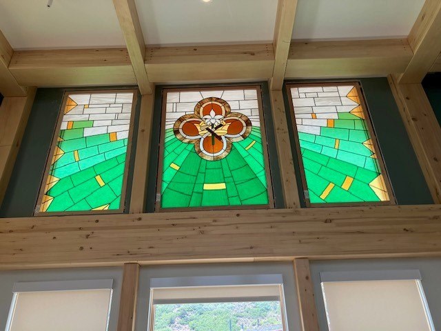 A stained glass window with a flower design is in the center of a wooden frame.