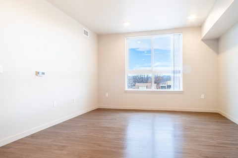 Empty room with a large window and wooden flooring.at All Saints Apartments, DENVER, 80219