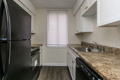 A black refrigerator sits in a kitchen with white cabinets and a granite countertop.