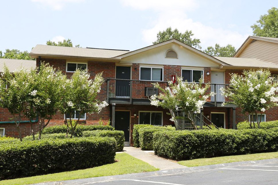 a brick house with bushes and trees in front of it
