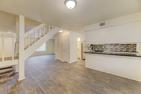 A spacious room with wooden flooring and a staircase on the left side.