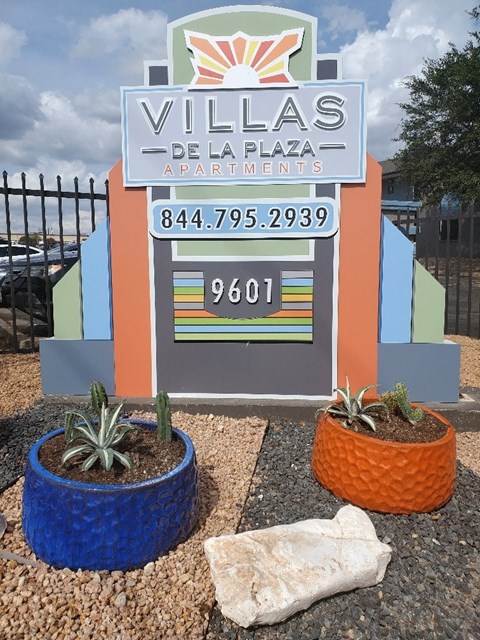 A sign for Villas De La Plaza Apartments with a phone number and a zip code.